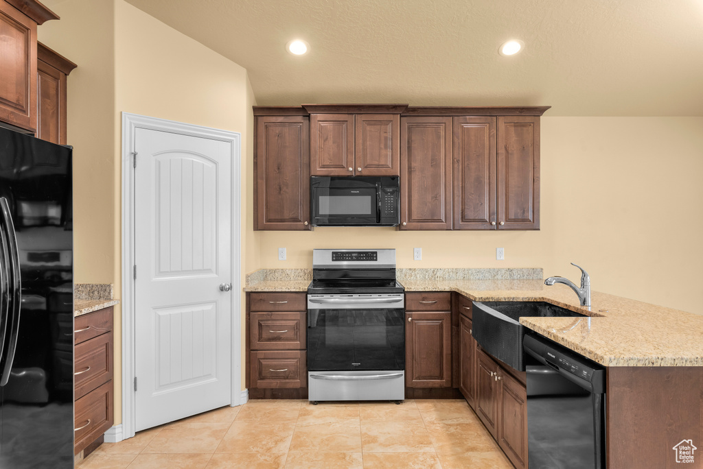 Kitchen featuring kitchen peninsula, light stone countertops, black appliances, sink, and light tile floors