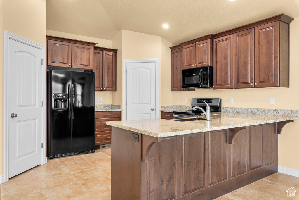 Kitchen with light stone countertops, kitchen peninsula, vaulted ceiling, light tile flooring, and black appliances
