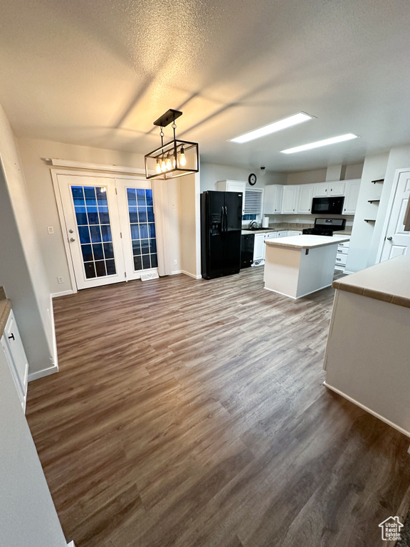 Kitchen with a kitchen island, white cabinetry, black appliances, hardwood / wood-style flooring, and pendant lighting