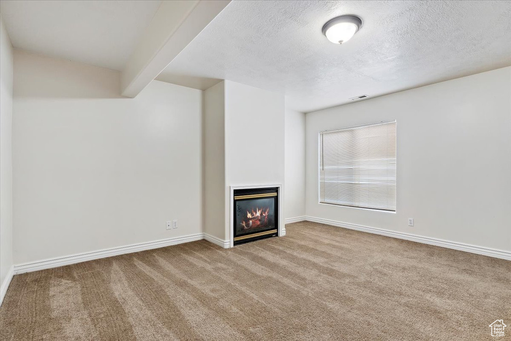 Unfurnished living room featuring carpet flooring, beamed ceiling, and a textured ceiling