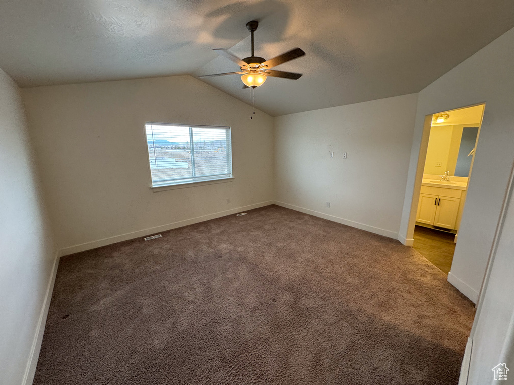 Unfurnished bedroom with ceiling fan, sink, ensuite bath, carpet flooring, and vaulted ceiling