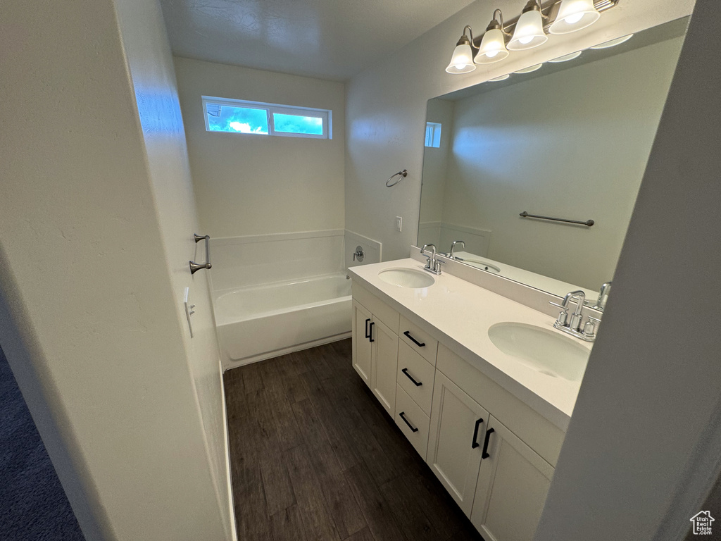 Bathroom with wood-type flooring, a tub, oversized vanity, and dual sinks