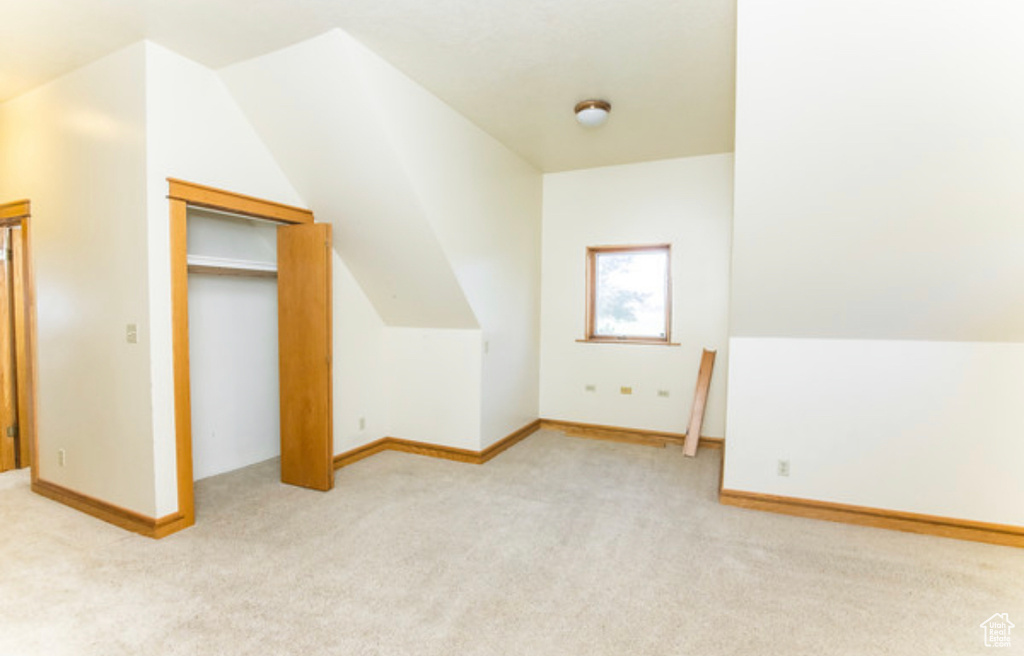 Unfurnished bedroom featuring light carpet, a closet, and lofted ceiling