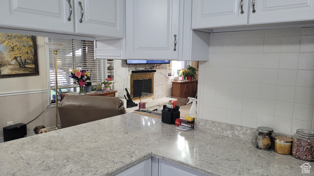 Kitchen featuring backsplash, white cabinetry, a premium fireplace, and light stone countertops