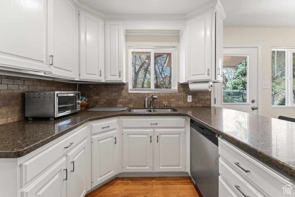 Kitchen with sink, dishwasher, tasteful backsplash, light wood-type flooring, and white cabinetry