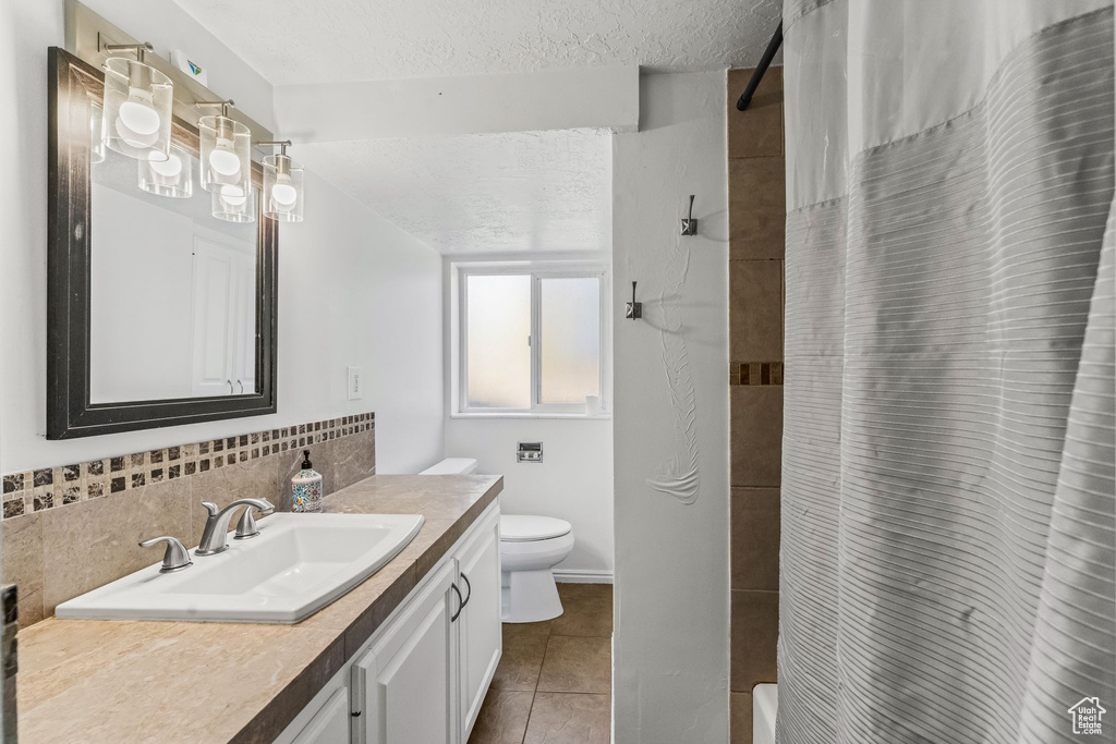 Bathroom with tile floors, vanity with extensive cabinet space, tasteful backsplash, and toilet