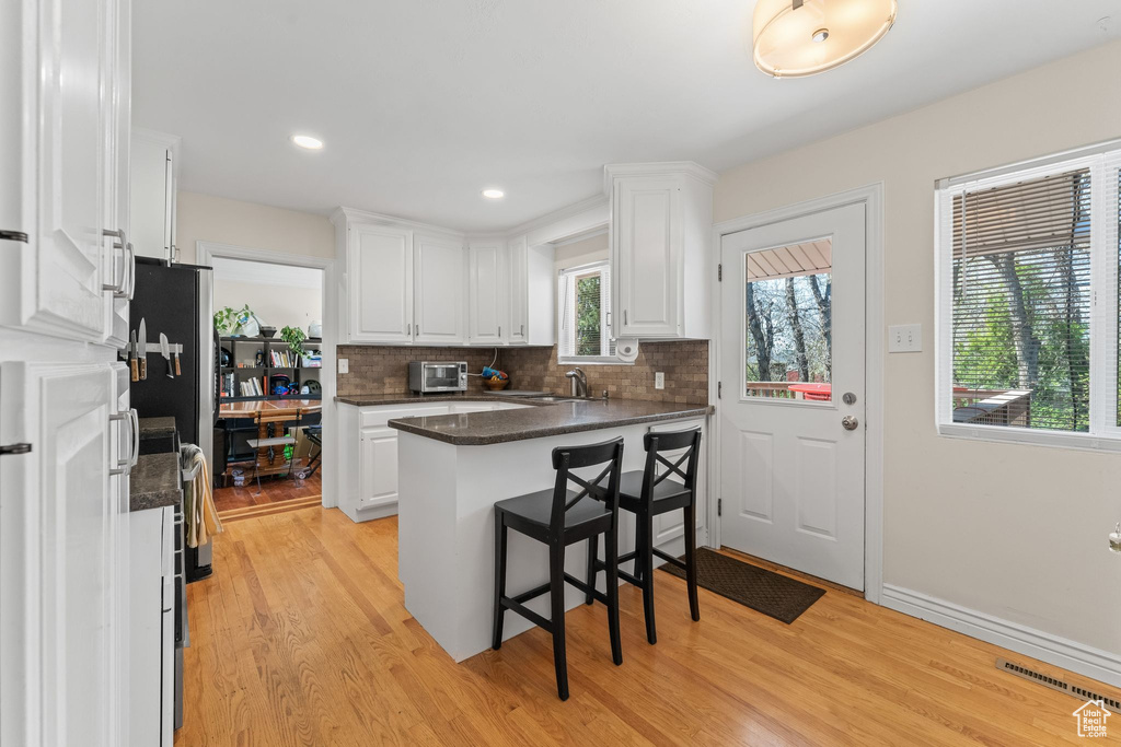 Kitchen featuring backsplash, light hardwood / wood-style floors, white cabinets, and a kitchen bar