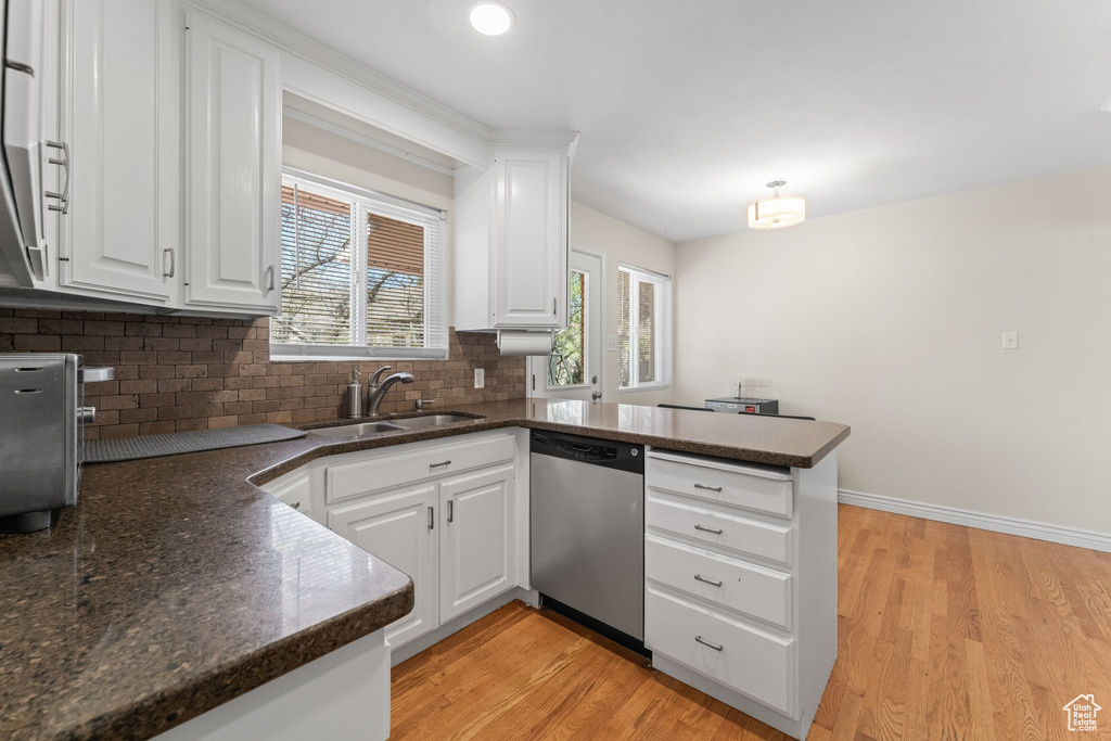 Kitchen with kitchen peninsula, light hardwood / wood-style flooring, dishwasher, white cabinetry, and sink