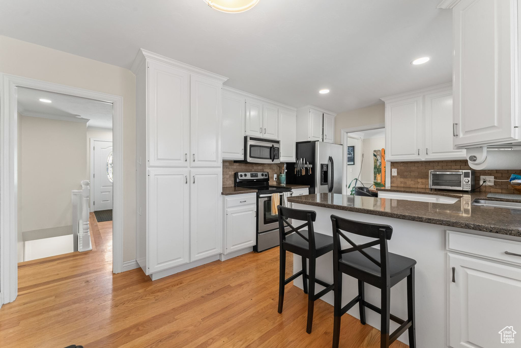 Kitchen with backsplash, appliances with stainless steel finishes, light hardwood / wood-style flooring, and white cabinets