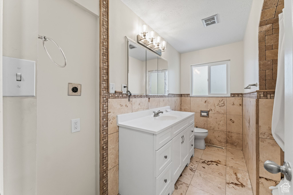 Bathroom with tile flooring, tile walls, a textured ceiling, toilet, and vanity