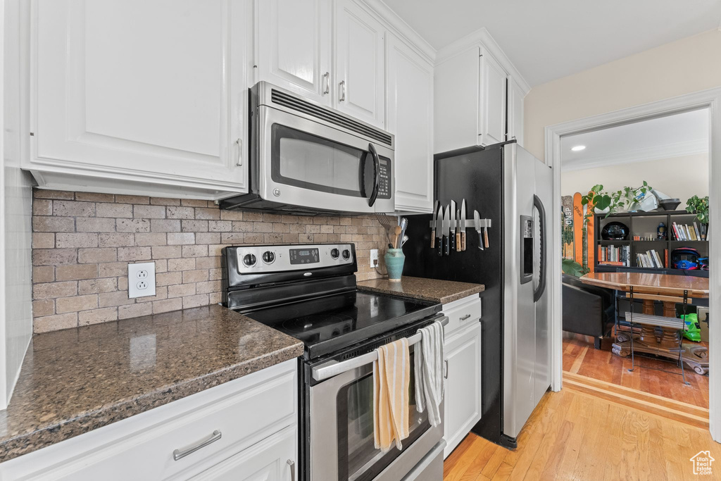 Kitchen with white cabinets, tasteful backsplash, stainless steel appliances, light hardwood / wood-style flooring, and dark stone countertops