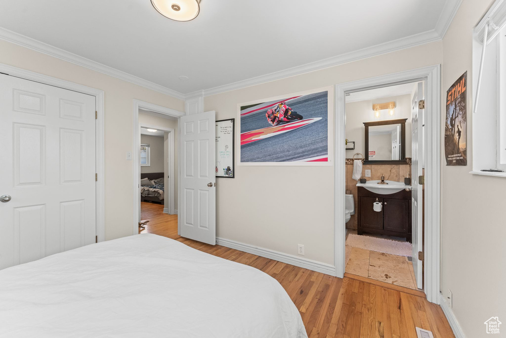 Bedroom with ornamental molding, connected bathroom, light hardwood / wood-style flooring, and sink