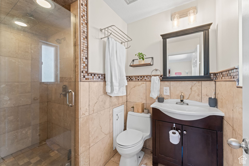 Bathroom featuring a shower with door, tile walls, vanity, and toilet