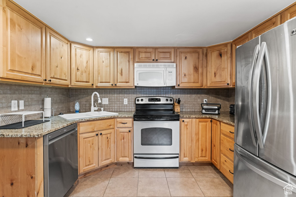 Kitchen with backsplash, appliances with stainless steel finishes, sink, and light stone counters
