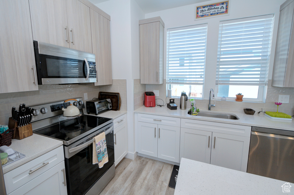 Kitchen featuring white cabinets, light hardwood / wood-style flooring, backsplash, stainless steel appliances, and sink