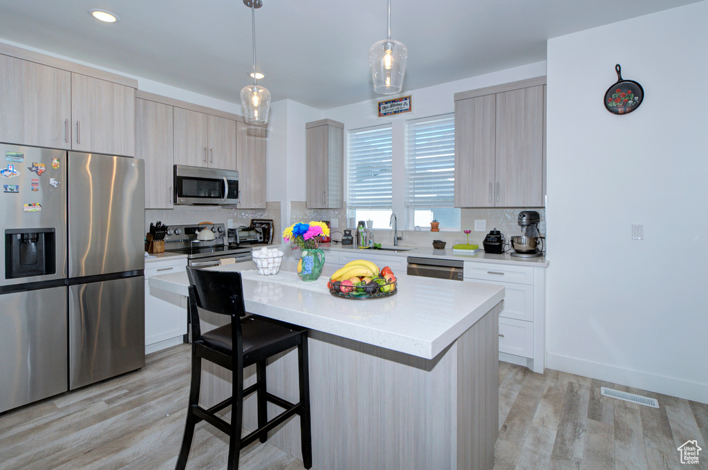 Kitchen with light hardwood / wood-style flooring, tasteful backsplash, stainless steel appliances, and a center island
