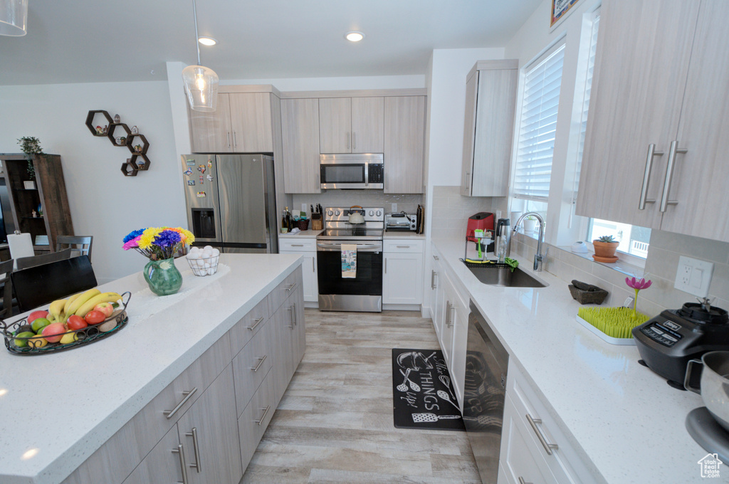 Kitchen with sink, light hardwood / wood-style floors, backsplash, stainless steel appliances, and pendant lighting