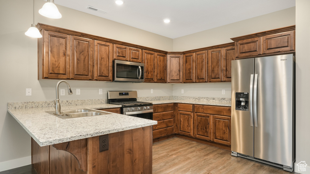 Kitchen featuring light stone countertops, appliances with stainless steel finishes, light hardwood / wood-style flooring, hanging light fixtures, and sink