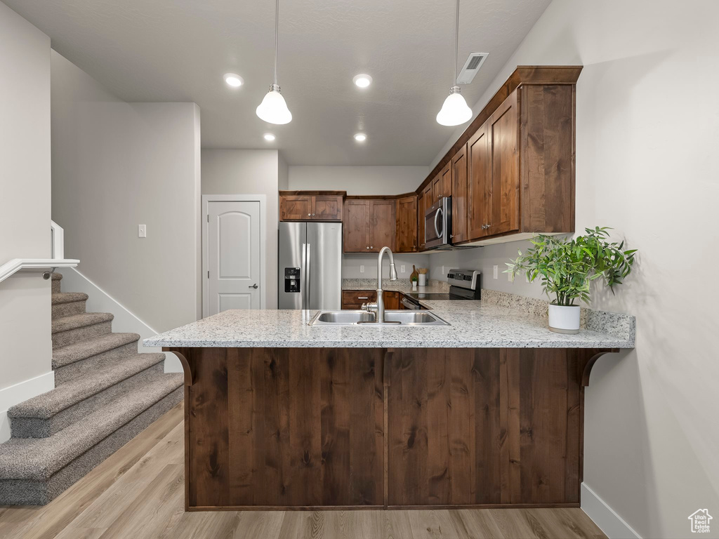 Kitchen with light wood-type flooring, kitchen peninsula, and appliances with stainless steel finishes