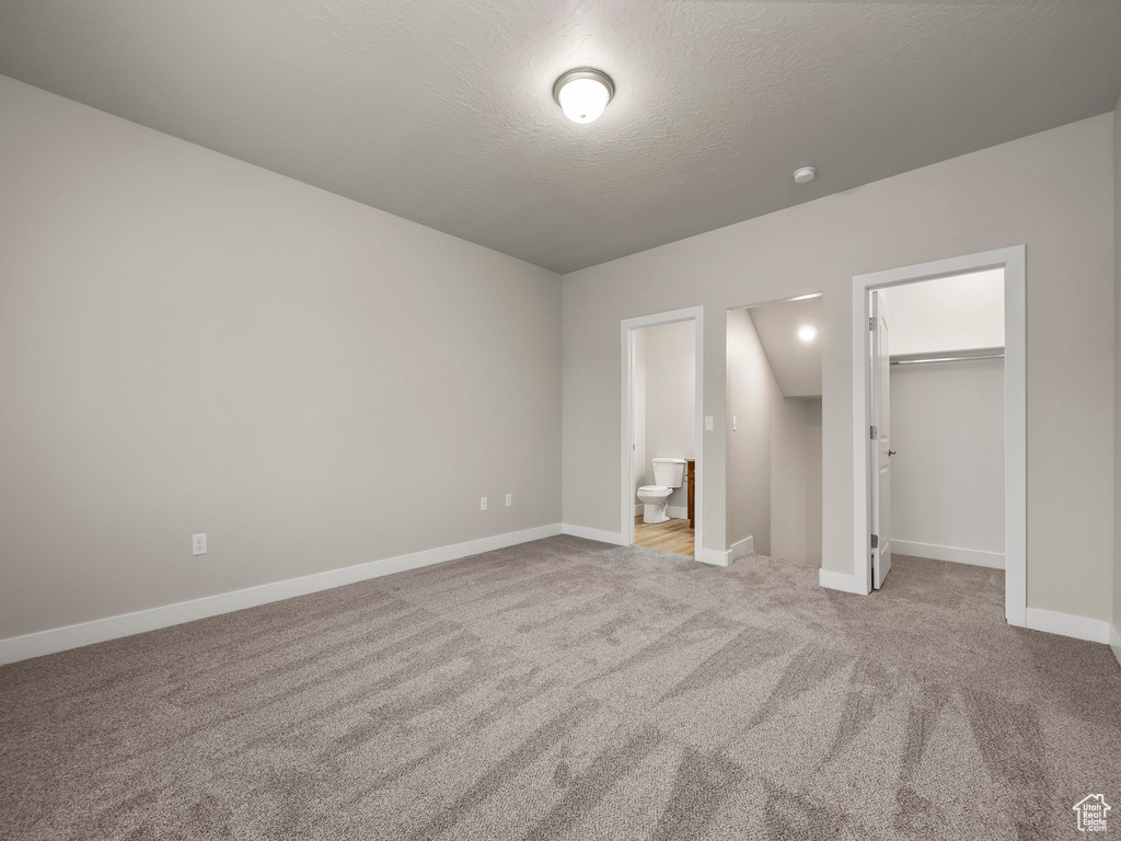 Unfurnished bedroom featuring light carpet, a textured ceiling, a spacious closet, connected bathroom, and a closet