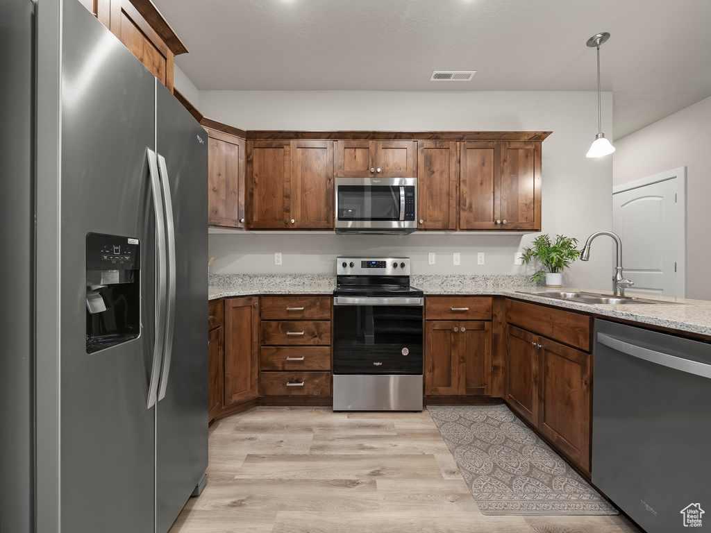 Kitchen featuring sink, hanging light fixtures, stainless steel appliances, light stone counters, and light wood-type flooring