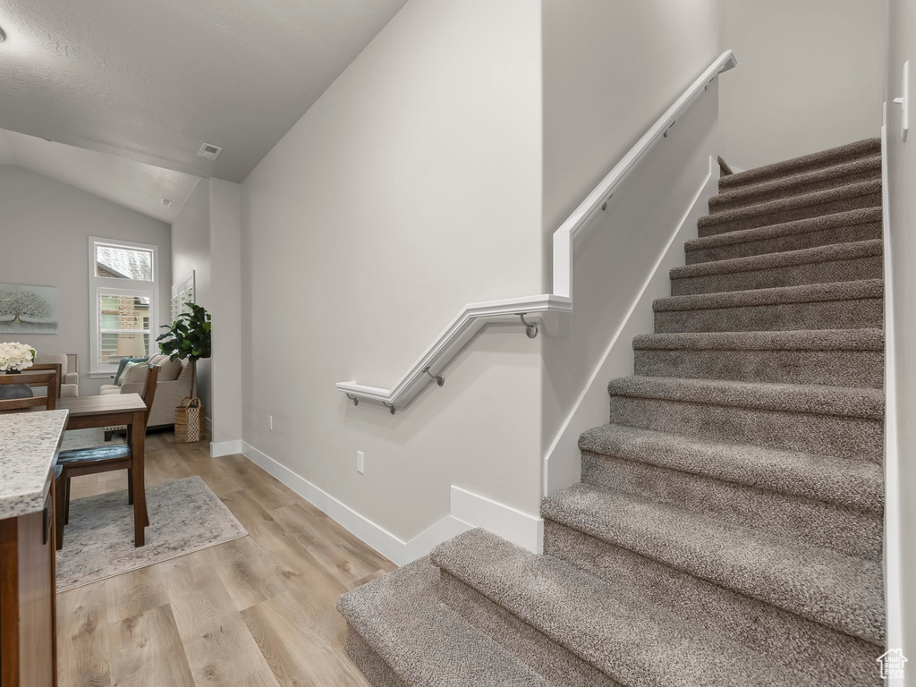 Stairs featuring wood-type flooring and vaulted ceiling