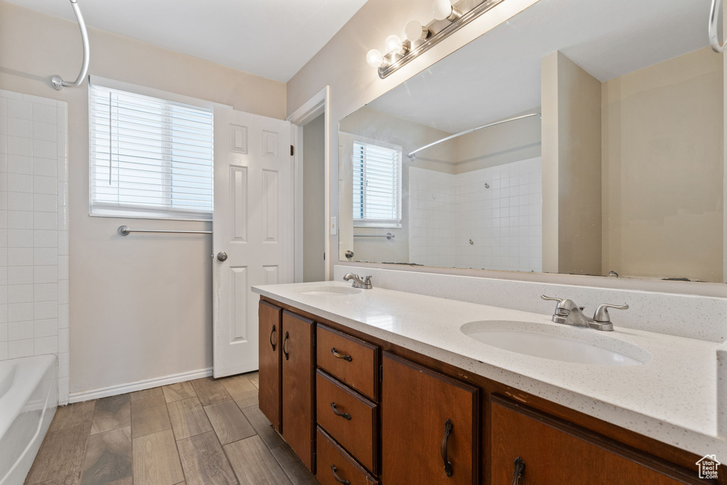 Bathroom with tiled shower / bath combo, double vanity, and wood-type flooring