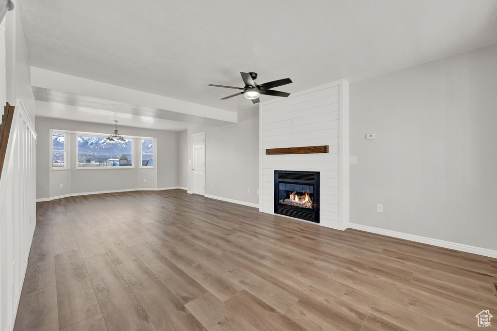 Unfurnished living room featuring ceiling fan with notable chandelier, hardwood / wood-style floors, and a large fireplace