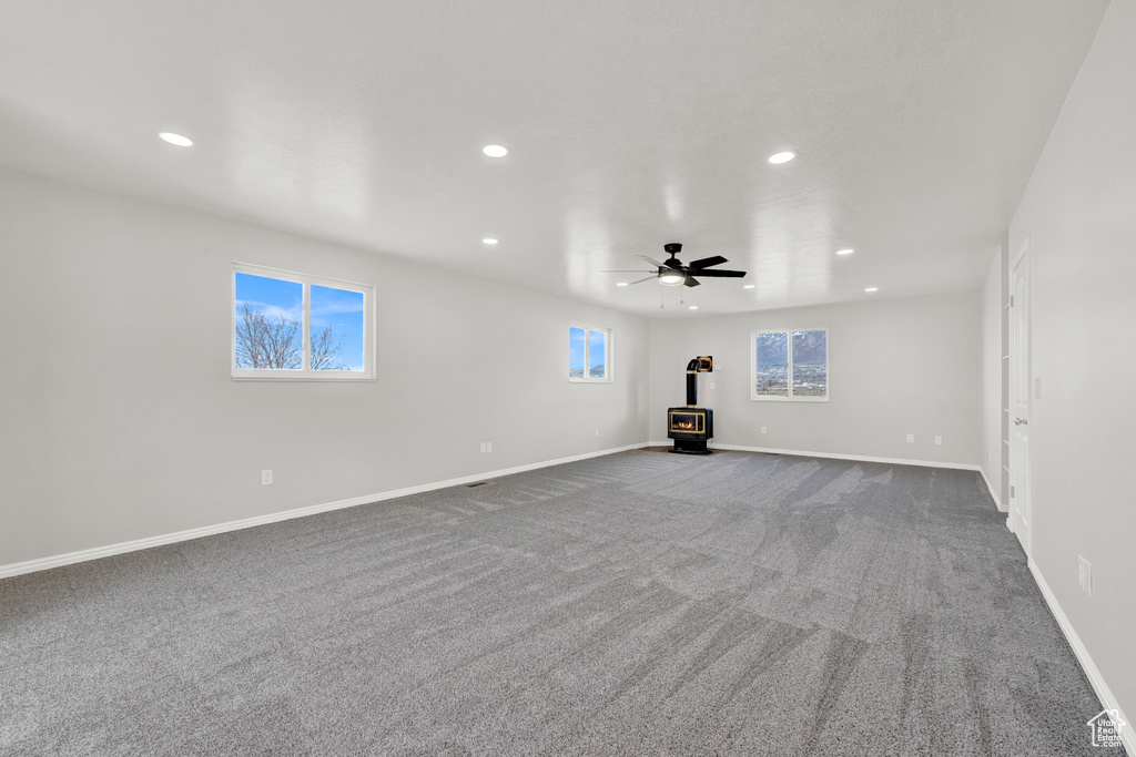 Empty room with ceiling fan, a wood stove, and dark colored carpet