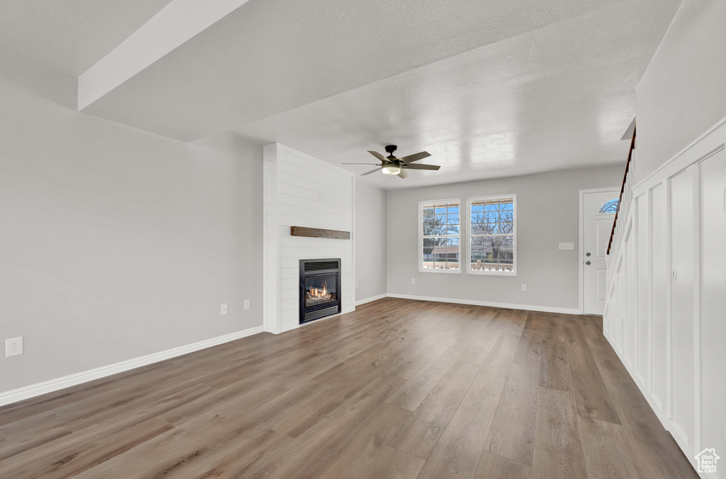 Unfurnished living room featuring dark hardwood / wood-style flooring, ceiling fan, and a fireplace