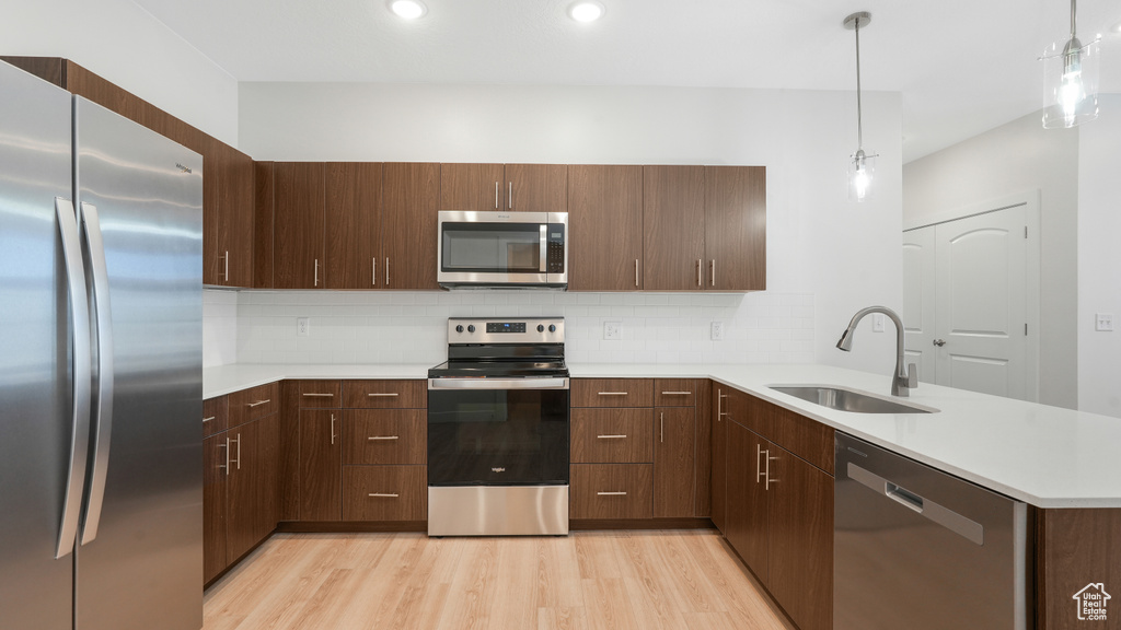 Kitchen with sink, stainless steel appliances, light hardwood / wood-style floors, and decorative light fixtures