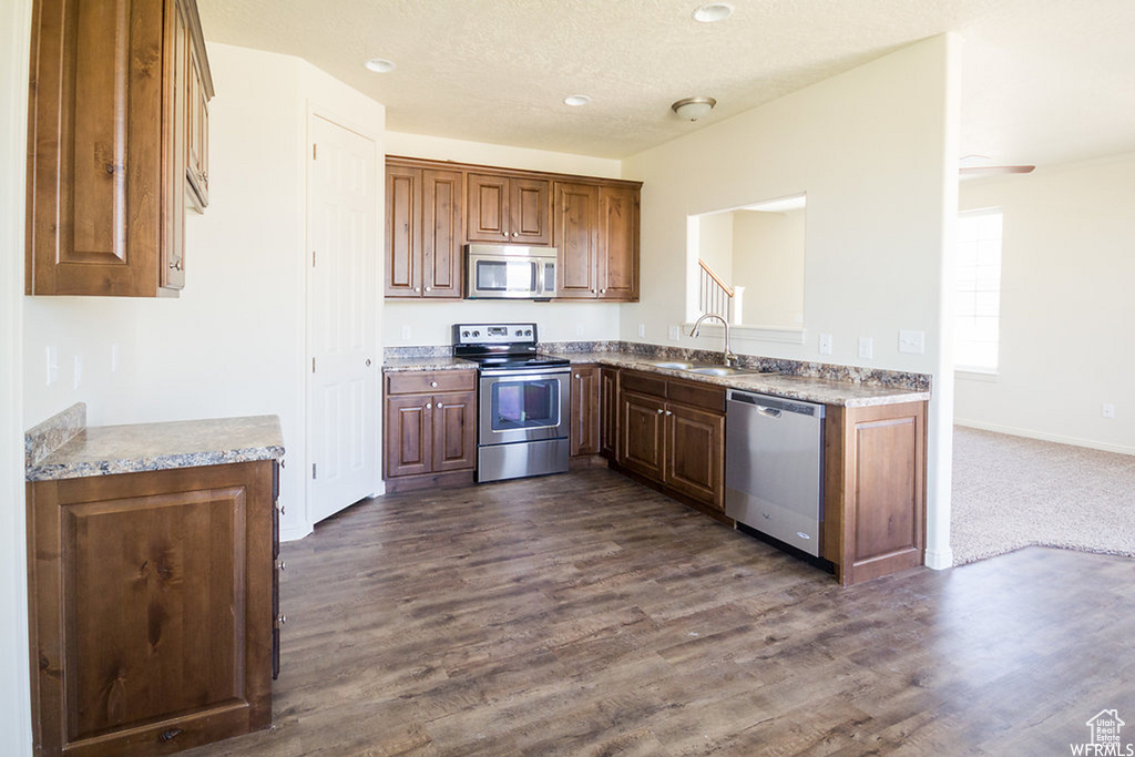 Kitchen with sink, appliances with stainless steel finishes, dark carpet, and light stone countertops