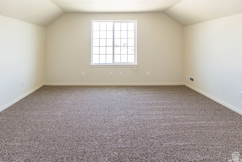 Bonus room with light carpet and vaulted ceiling
