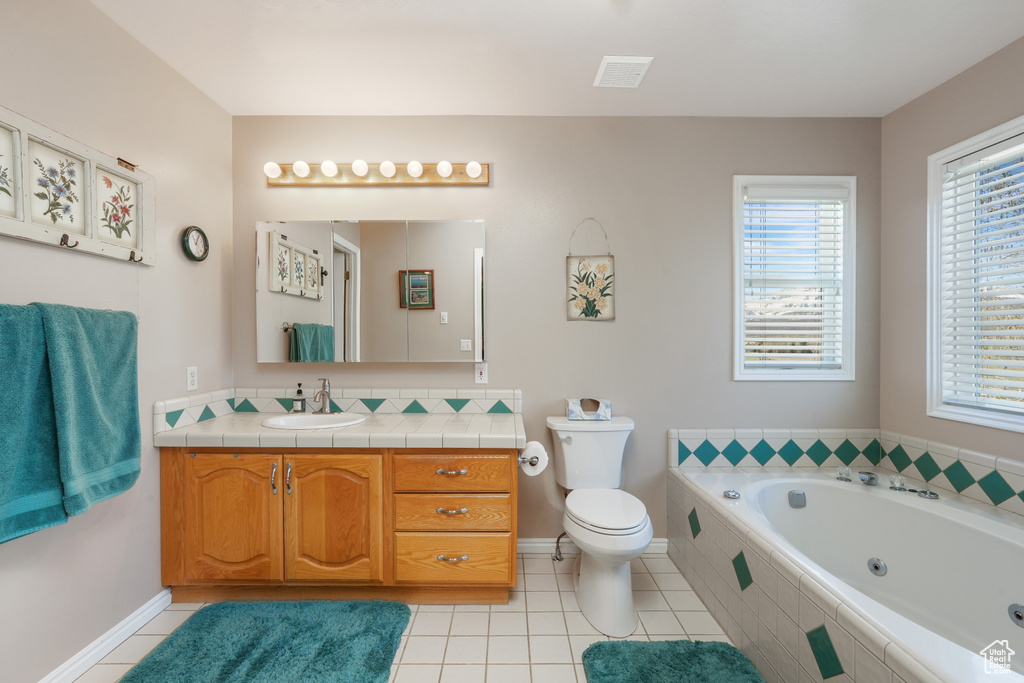 Bathroom with tile floors, vanity with extensive cabinet space, toilet, and tiled bath