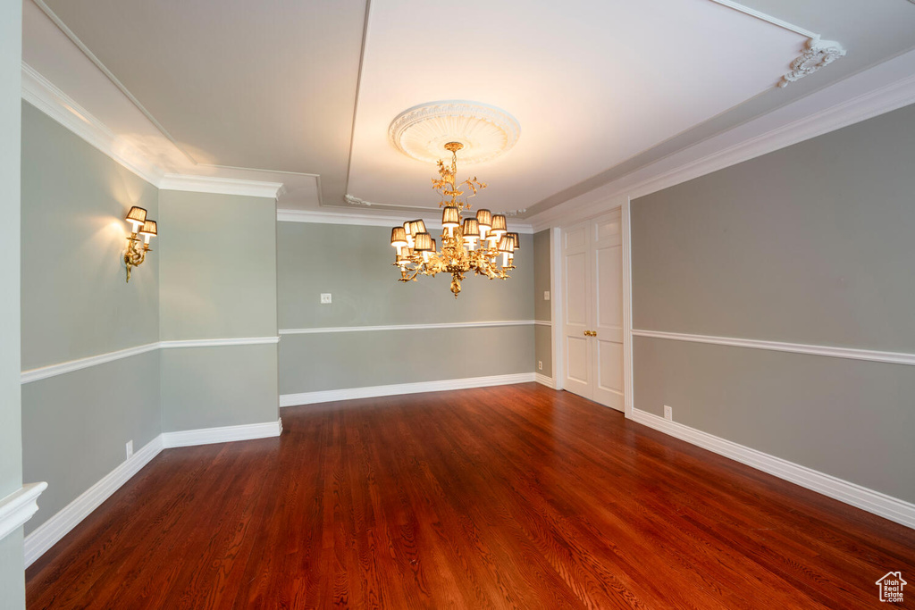 Empty room with crown molding, a chandelier, and dark hardwood / wood-style floors