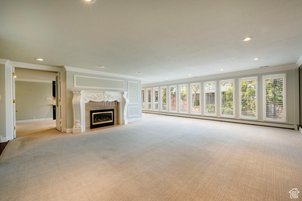 Unfurnished living room featuring light colored carpet, a wealth of natural light, crown molding, and a tiled fireplace