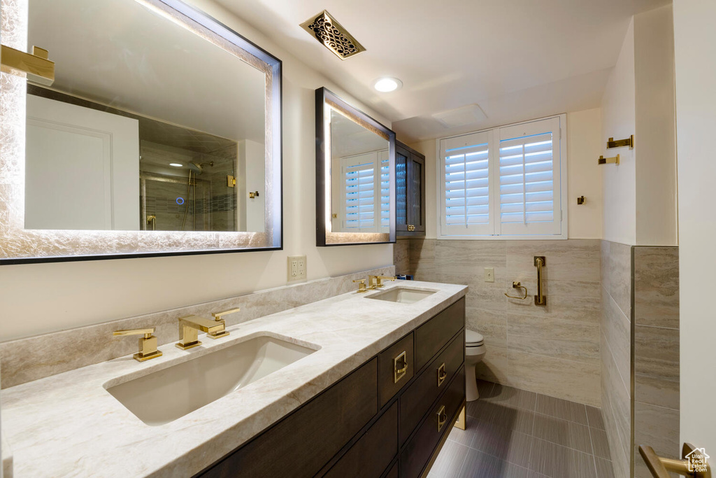 Bathroom featuring tile walls, double vanity, walk in shower, toilet, and tile floors