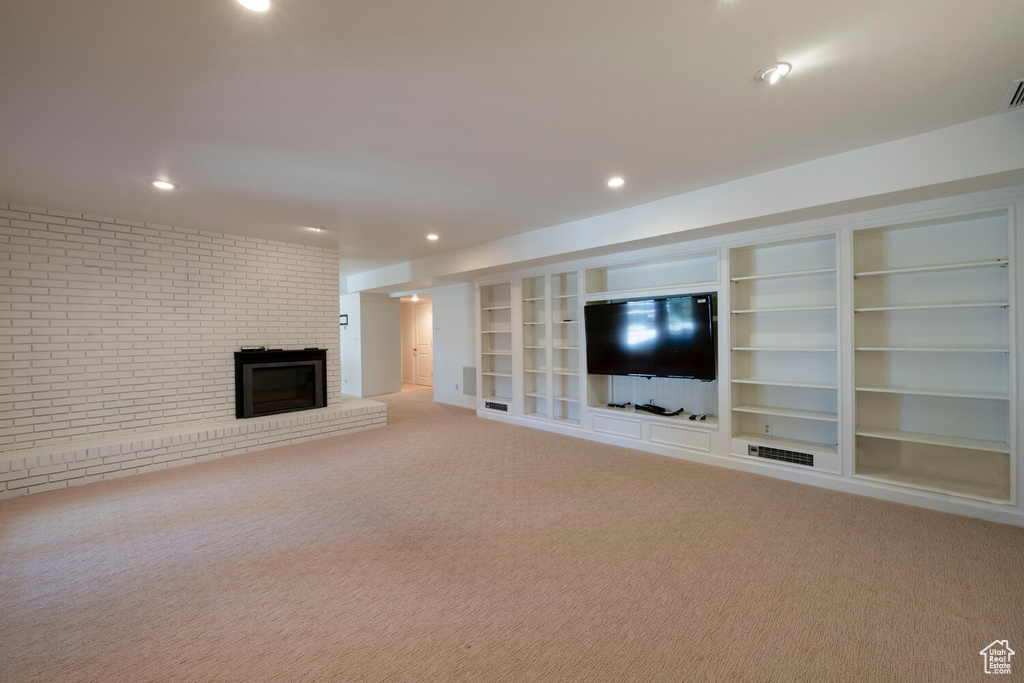 Unfurnished living room with light carpet, built in features, brick wall, and a fireplace
