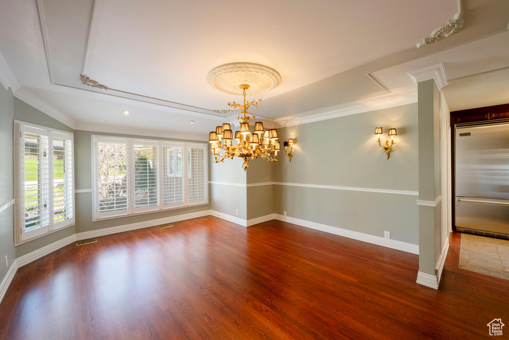Empty room featuring dark hardwood / wood-style flooring, crown molding, and a chandelier