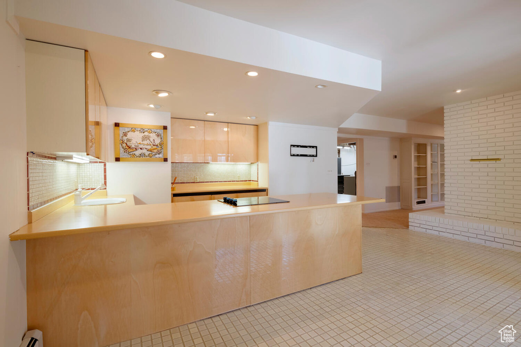 Kitchen featuring light tile flooring, a baseboard heating unit, sink, tasteful backsplash, and black electric cooktop