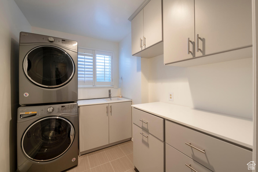 Laundry area with sink, stacked washer / dryer, cabinets, and light tile floors