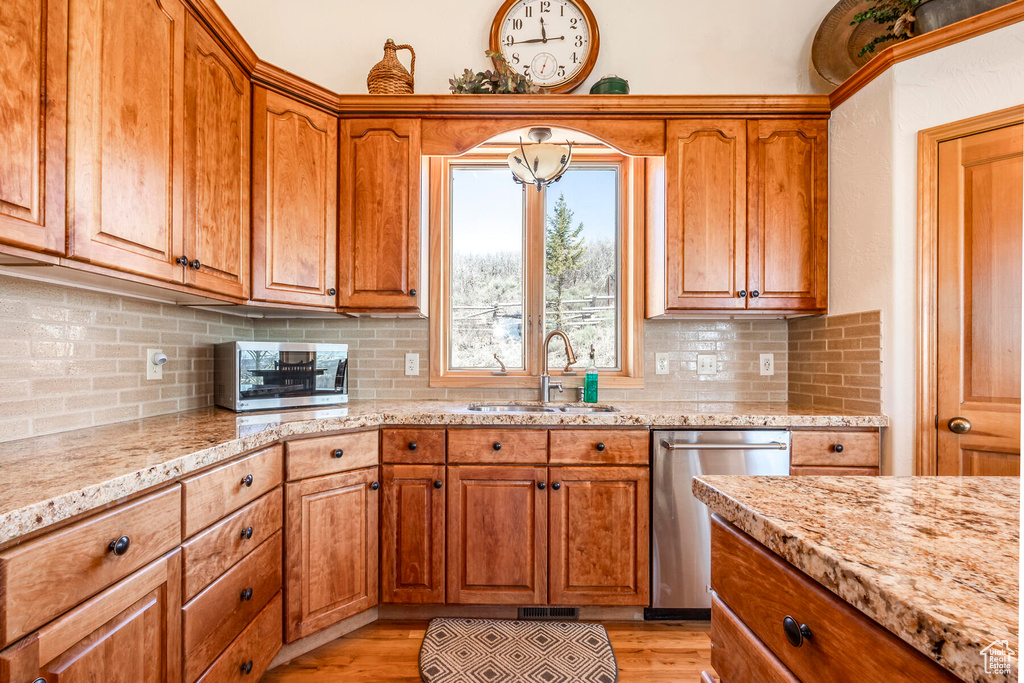 Kitchen with light stone countertops, backsplash, stainless steel appliances, sink, and light hardwood / wood-style floors