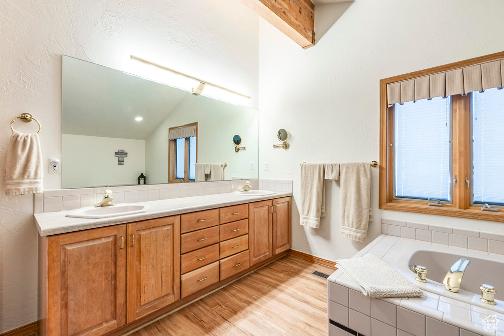 Bathroom featuring large vanity, vaulted ceiling, a relaxing tiled bath, hardwood / wood-style flooring, and dual sinks