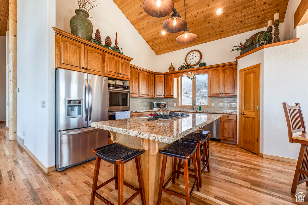 Kitchen with a center island, high vaulted ceiling, light hardwood / wood-style flooring, appliances with stainless steel finishes, and tasteful backsplash