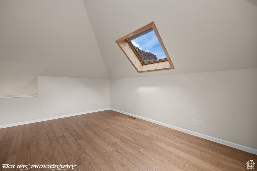 Additional living space with vaulted ceiling with skylight and light wood-type flooring