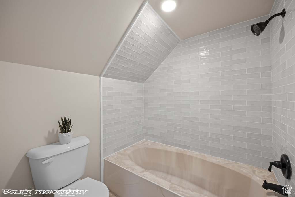 Bathroom featuring tiled shower / bath, toilet, and lofted ceiling