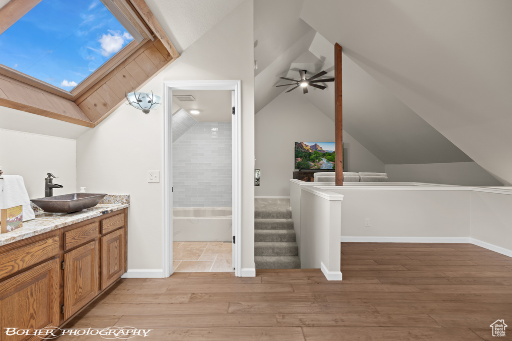 Bathroom with lofted ceiling with skylight, ceiling fan, vanity, and hardwood / wood-style flooring