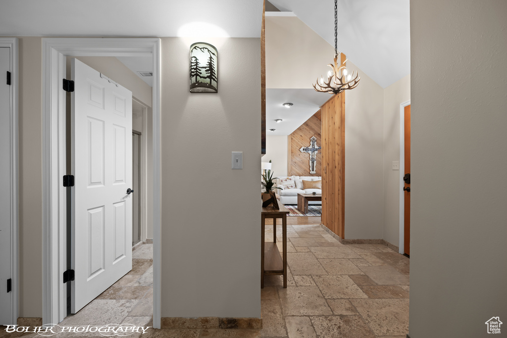 Hallway with vaulted ceiling, light tile flooring, and a chandelier