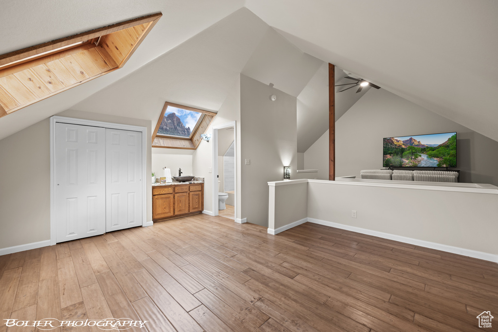 Bonus room with a skylight, light hardwood / wood-style flooring, ceiling fan, and high vaulted ceiling