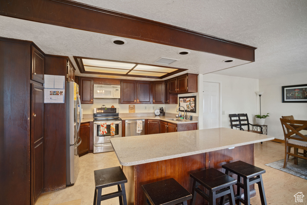 Kitchen featuring a kitchen bar, sink, appliances with stainless steel finishes, and a textured ceiling
